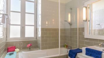 A bathroom with a bathtub, a sink, and a shower. There is a window with a view of the outside, and a towel rack with towels.