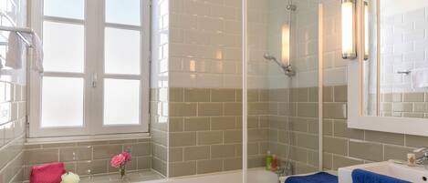 Un baño con bañera, lavamanos y ducha. Hay una ventana con vista al exterior, y un perchero con toallas.