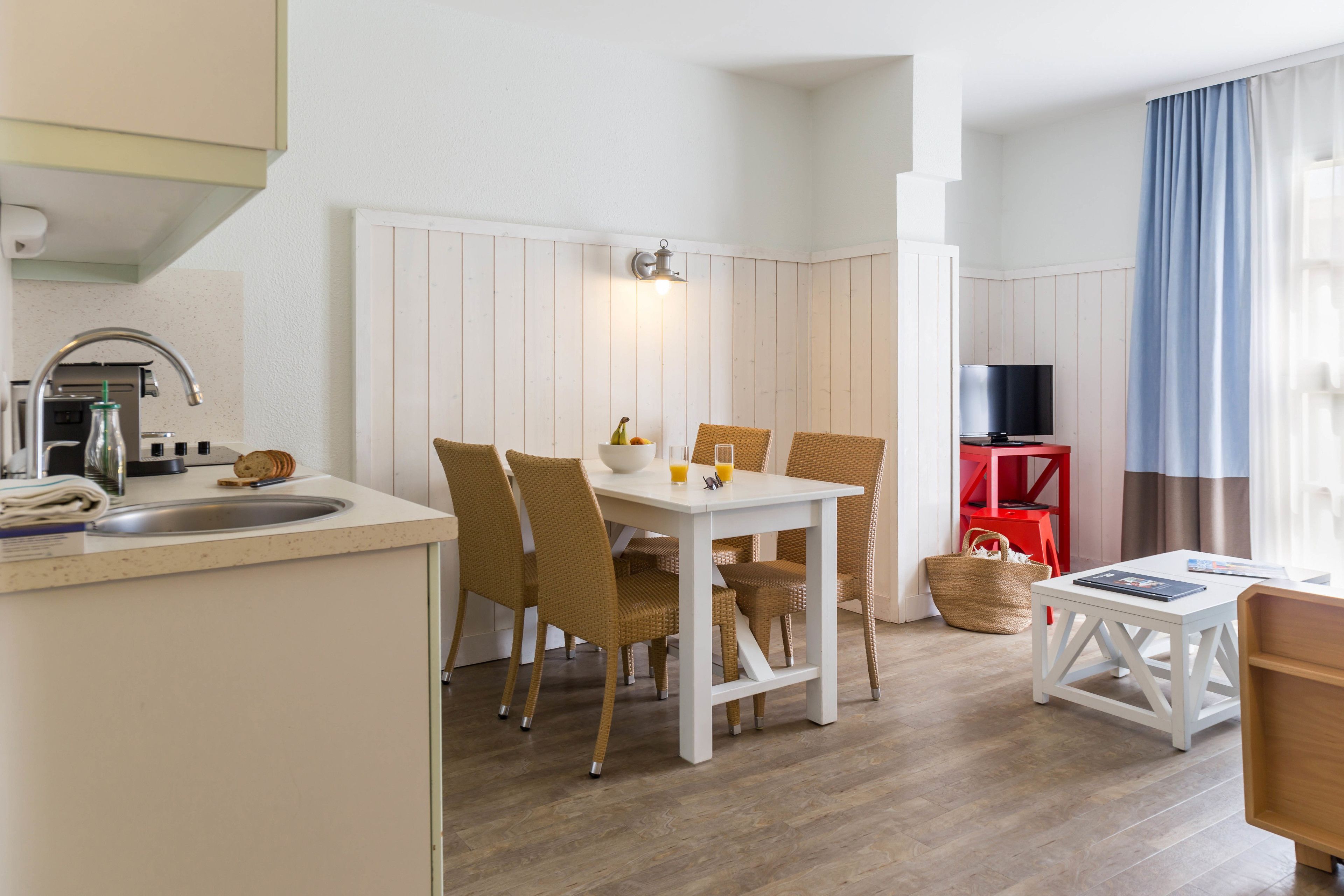 Cocina compacta con fregadero, estufa y comedor con sillas y mesa.