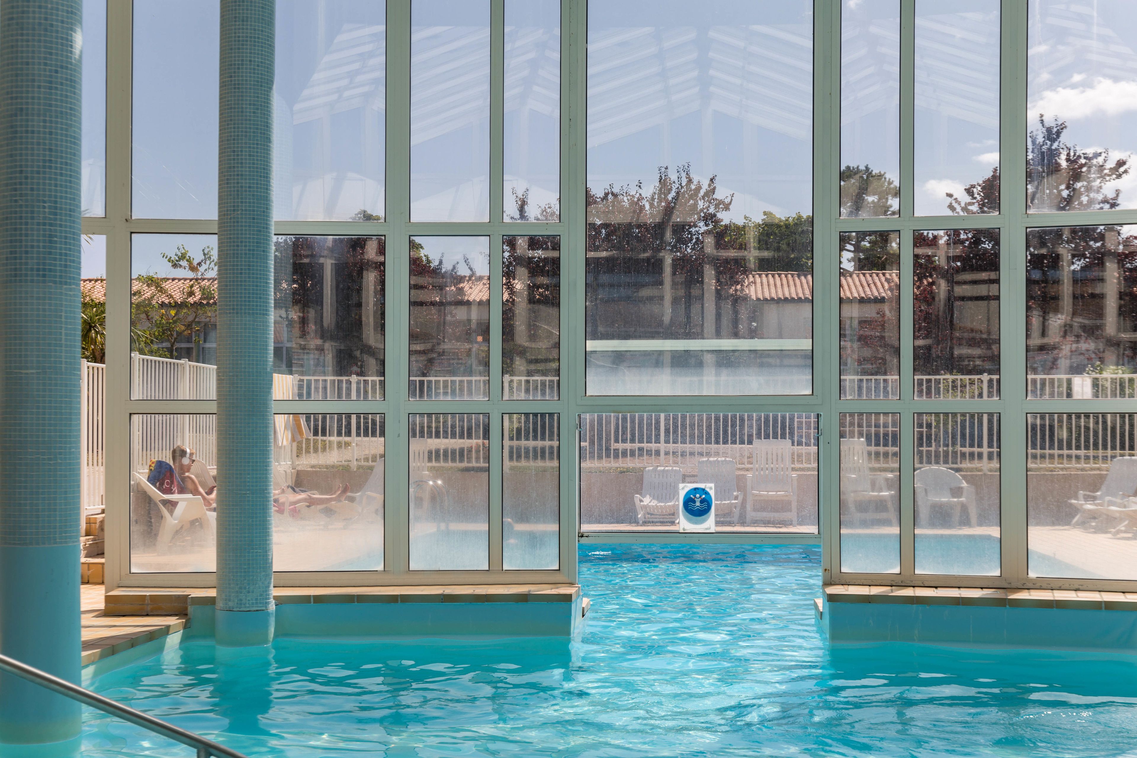 An indoor swimming pool with clear glass walls, a view of the outside, and a lifeguard chair.