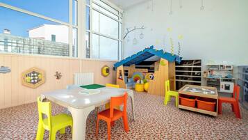 Una sala giochi per bambini con un'ampia finestra, strutture in legno e un tavolo bianco con sedie.