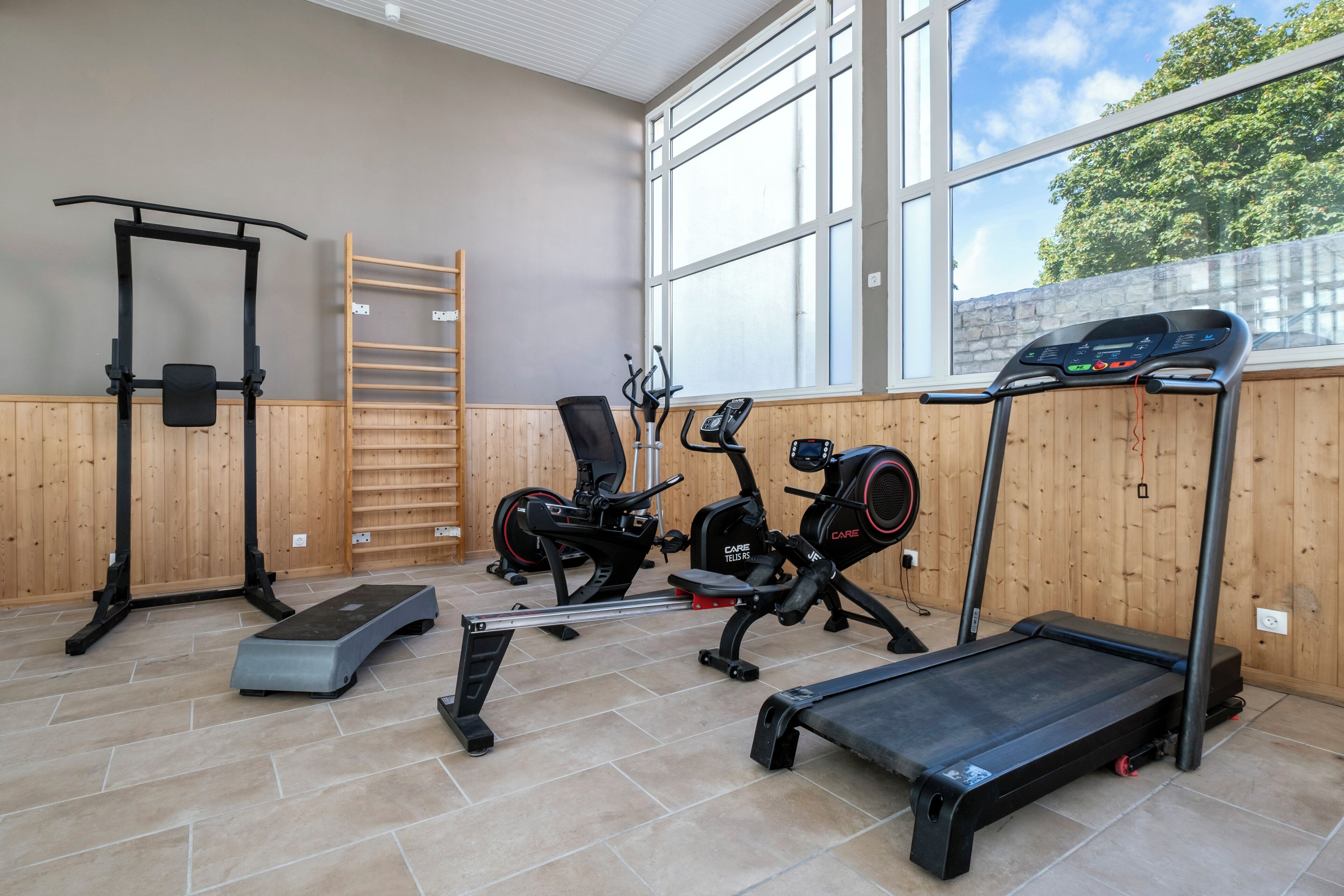A gym with exercise equipment including a pull-up bar, exercise bike, elliptical, treadmill, and a step platform.