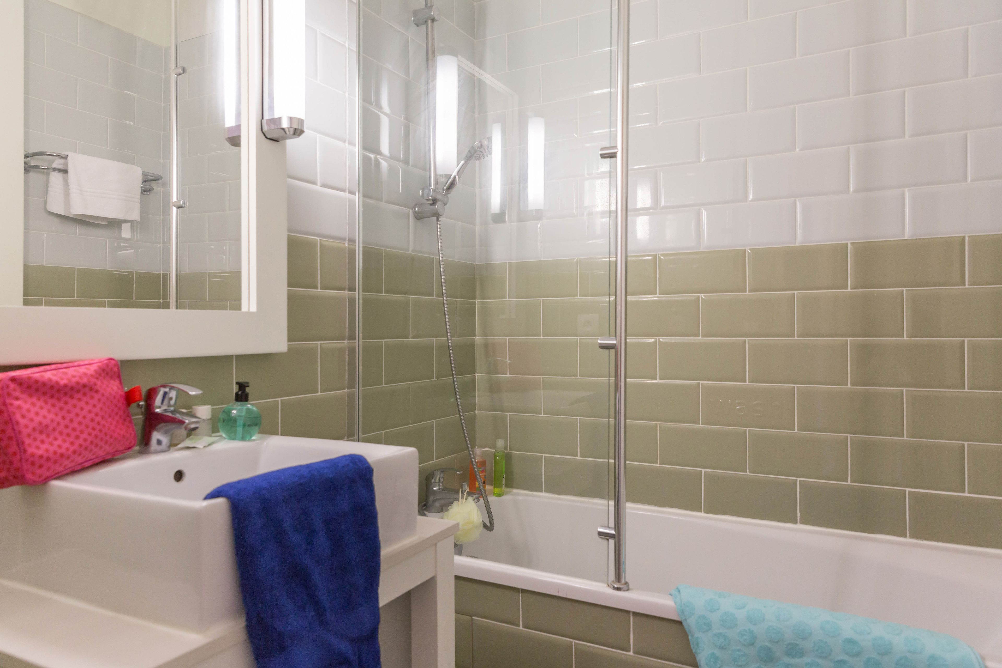 A bathroom with a white sink, a mirror, a shower with a glass door, and green tiled walls.