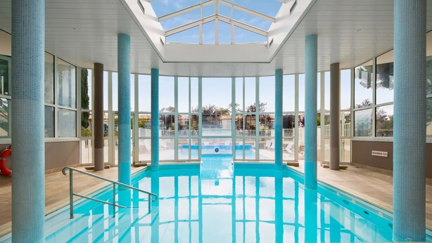 An indoor swimming pool with clear glass walls, a skylight, and a view of the outside. - Résidence Le Palais des Gouverneurs Pierre & Vacances (Saint-Martin-de-Re)