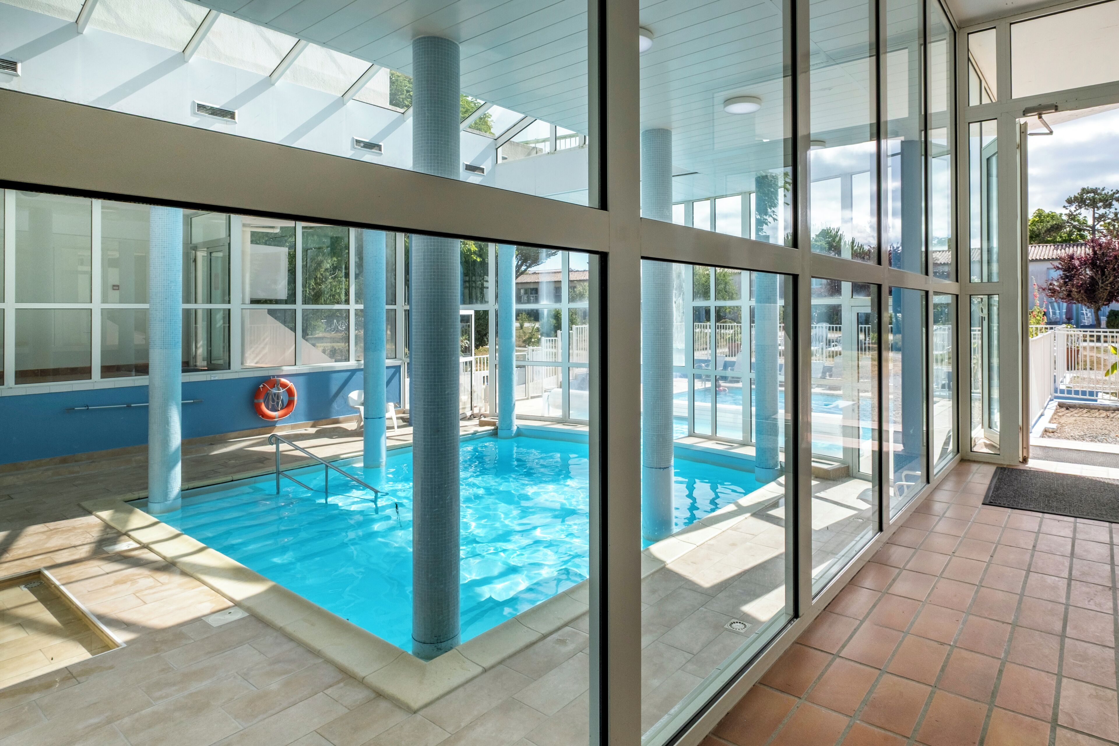 An indoor swimming pool with clear glass walls, a lifebuoy, and a tiled floor.