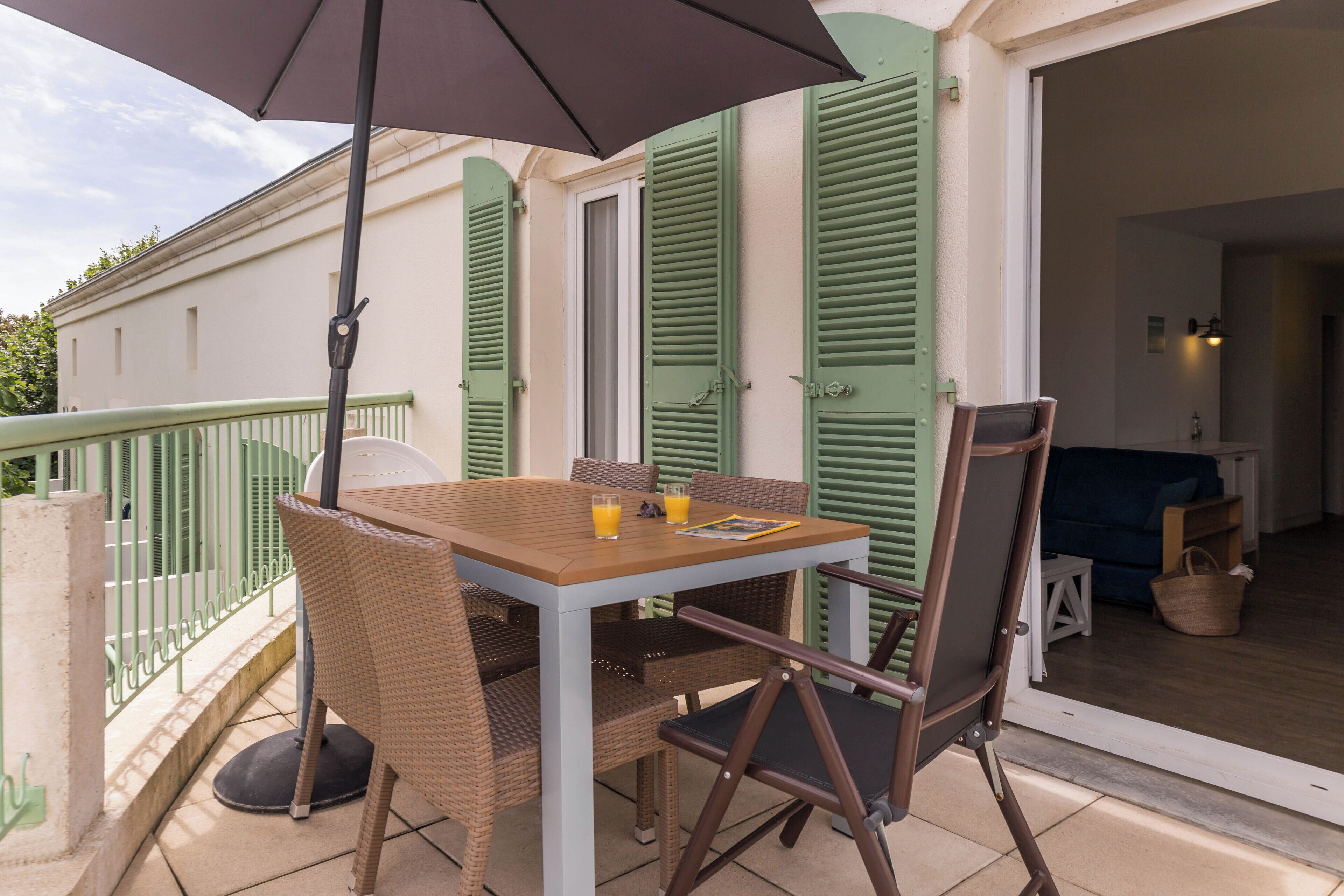 A balcony with a table and chairs, a table umbrella, and a view of the interior.
