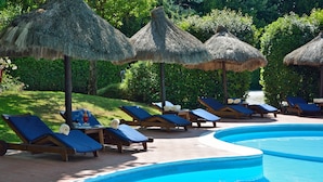 A poolside area with lounge chairs and thatched umbrellas, surrounded by greenery. - Hotel Calamidoro (Calcinaia)