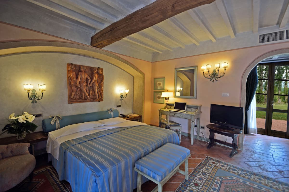 A bedroom with a bed, bedside tables, a desk with a chair, a television, and a large window.