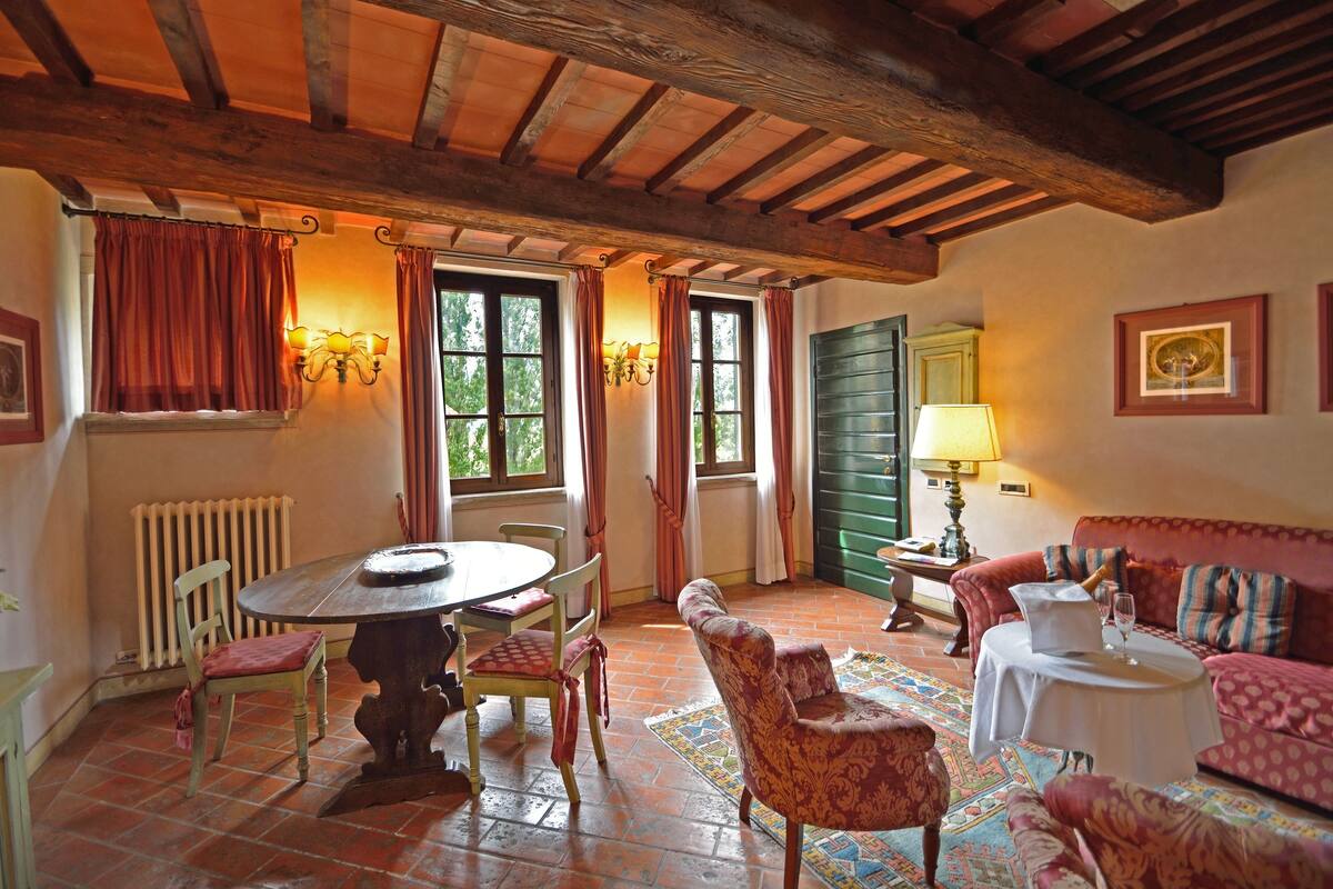 A cozy room with a wooden ceiling, a dining table with chairs, a sofa, and a lamp.