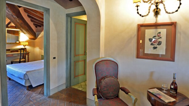 A hotel room with a bed, a chair, a table with a bottle and glass, and a framed picture on the wall. - Hotel Calamidoro (Calcinaia)