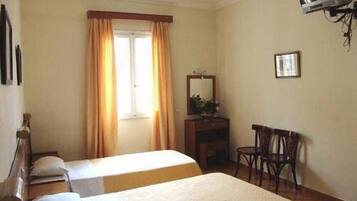 A hotel room with two beds, a desk, a chair, a television, and a window with curtains.