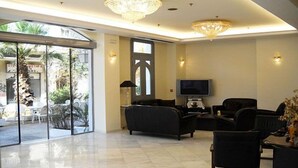 A modern hotel lobby with a large glass door leading to an outdoor area, a chandelier, and a flat-screen TV on a stand.
