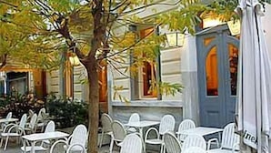 An outdoor seating area with white tables and chairs, a tree, and a building with a blue door.