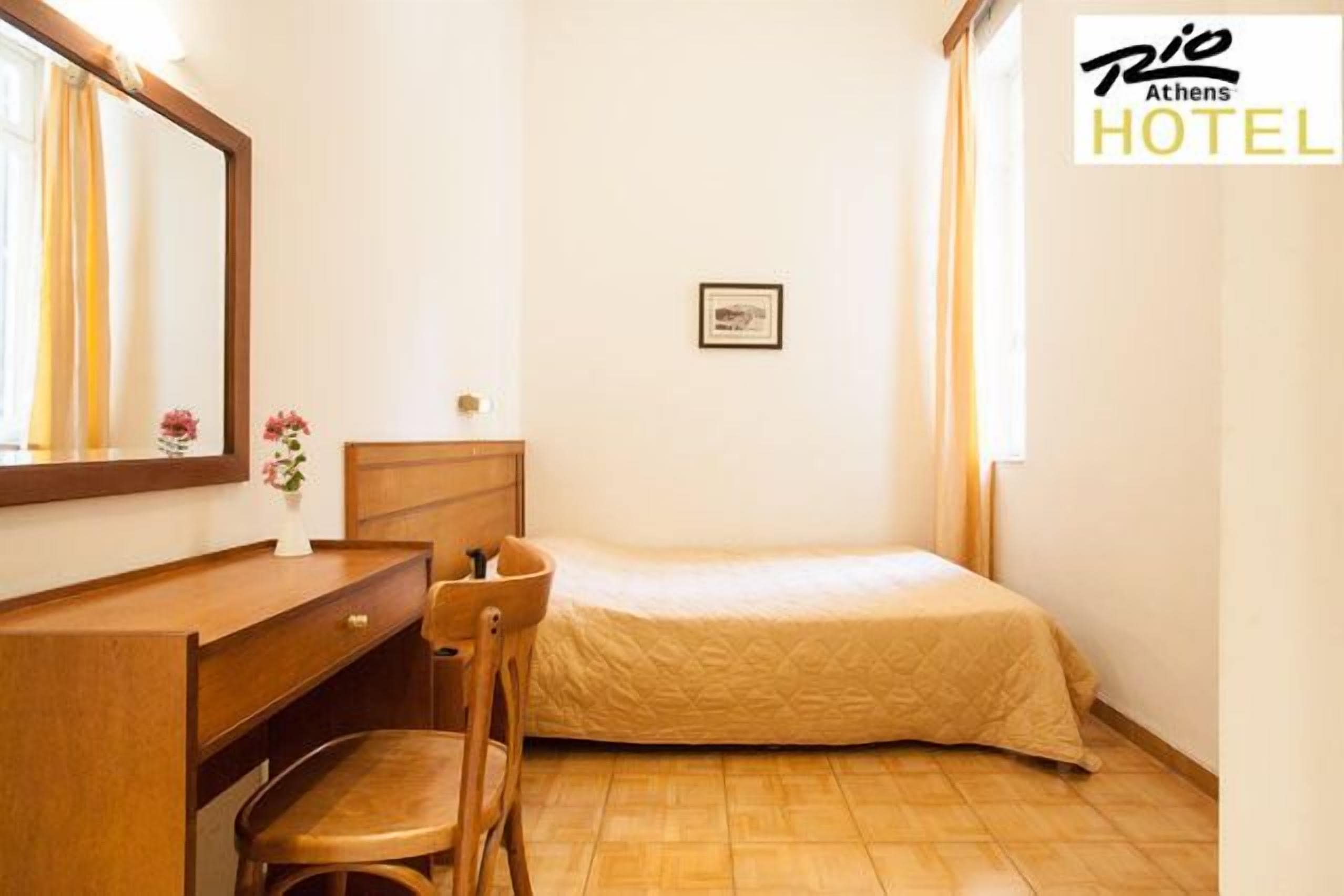 Een hotelkamer met een bed, een houten bureau met stoel, een spiegel en een klein, ingelijst schilderij aan de muur.