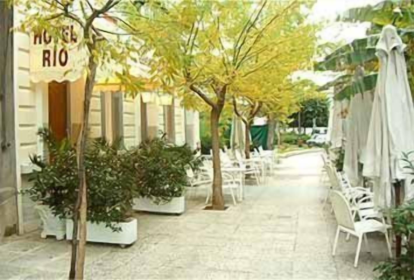 A courtyard with potted plants, outdoor seating, and a sign reading "HOTEL RIO".