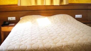 A hotel room with a bed, a nightstand, a telephone, and a wall socket.