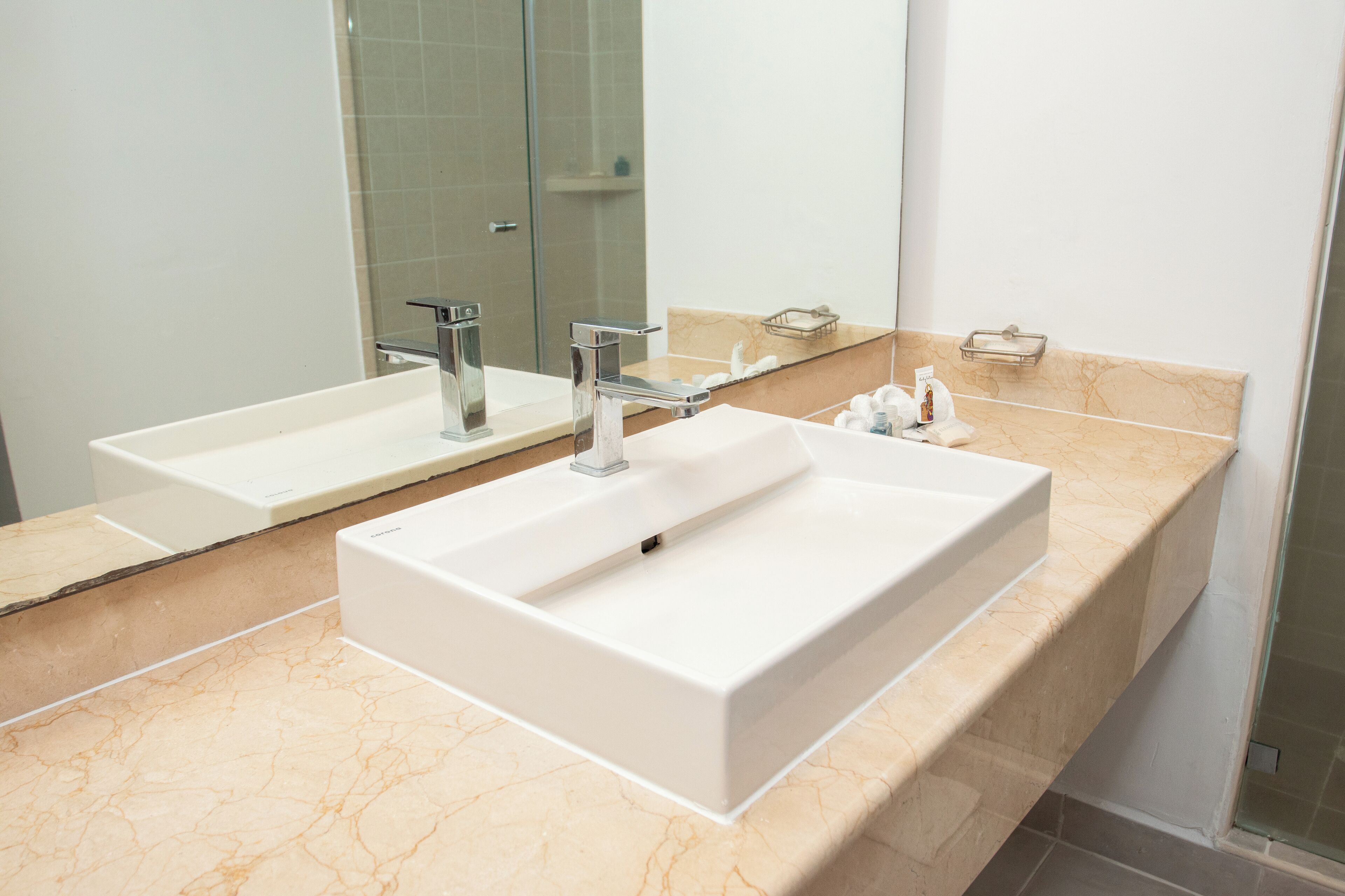 A bathroom with a large white sink, a mirror, and a shower area.