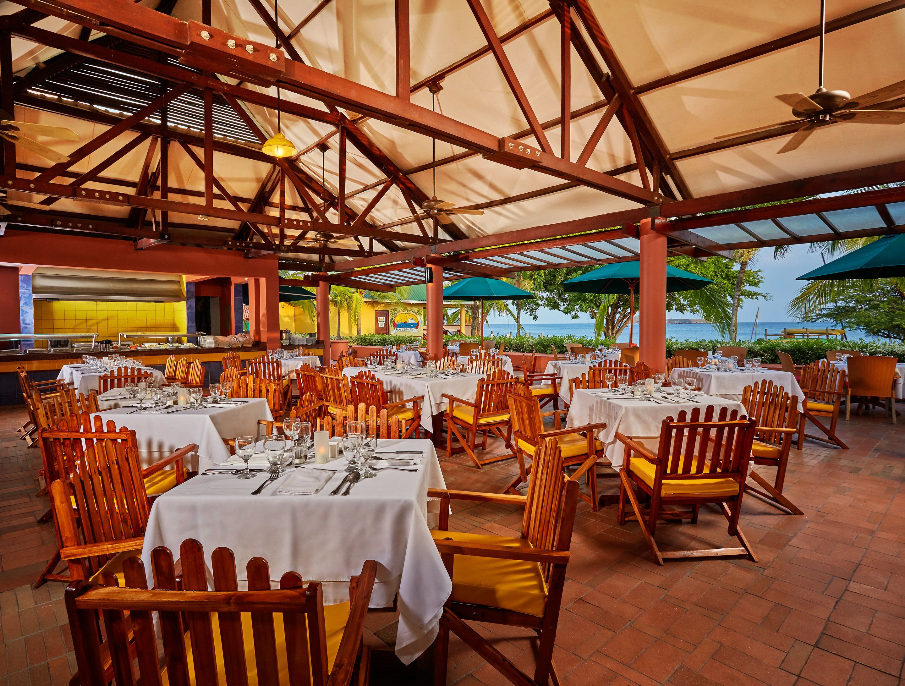 A restaurant with outdoor seating, white tablecloths, wooden chairs, and a view of the sea.