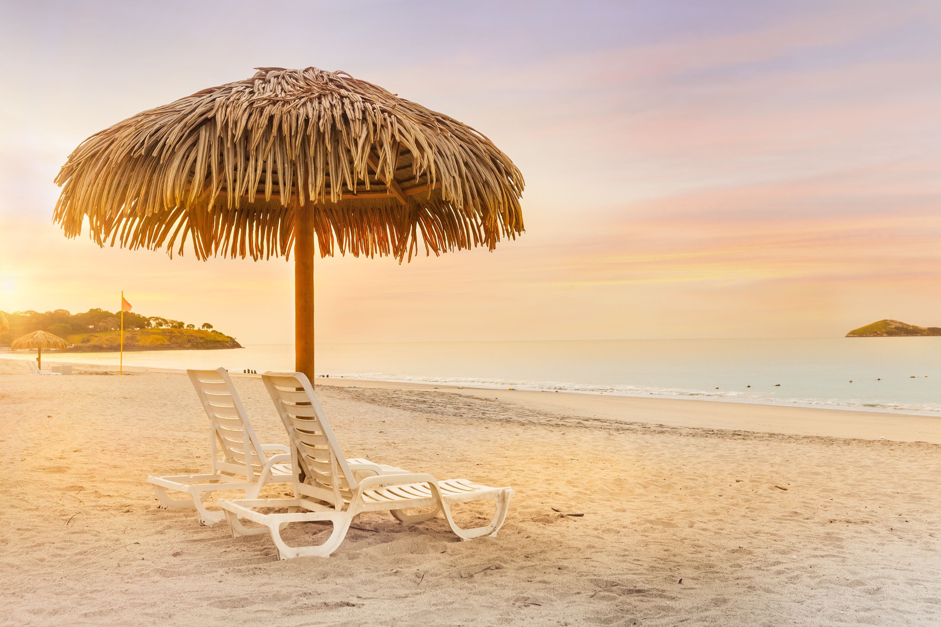 A beach scene with two white lounge chairs and a thatched umbrella.