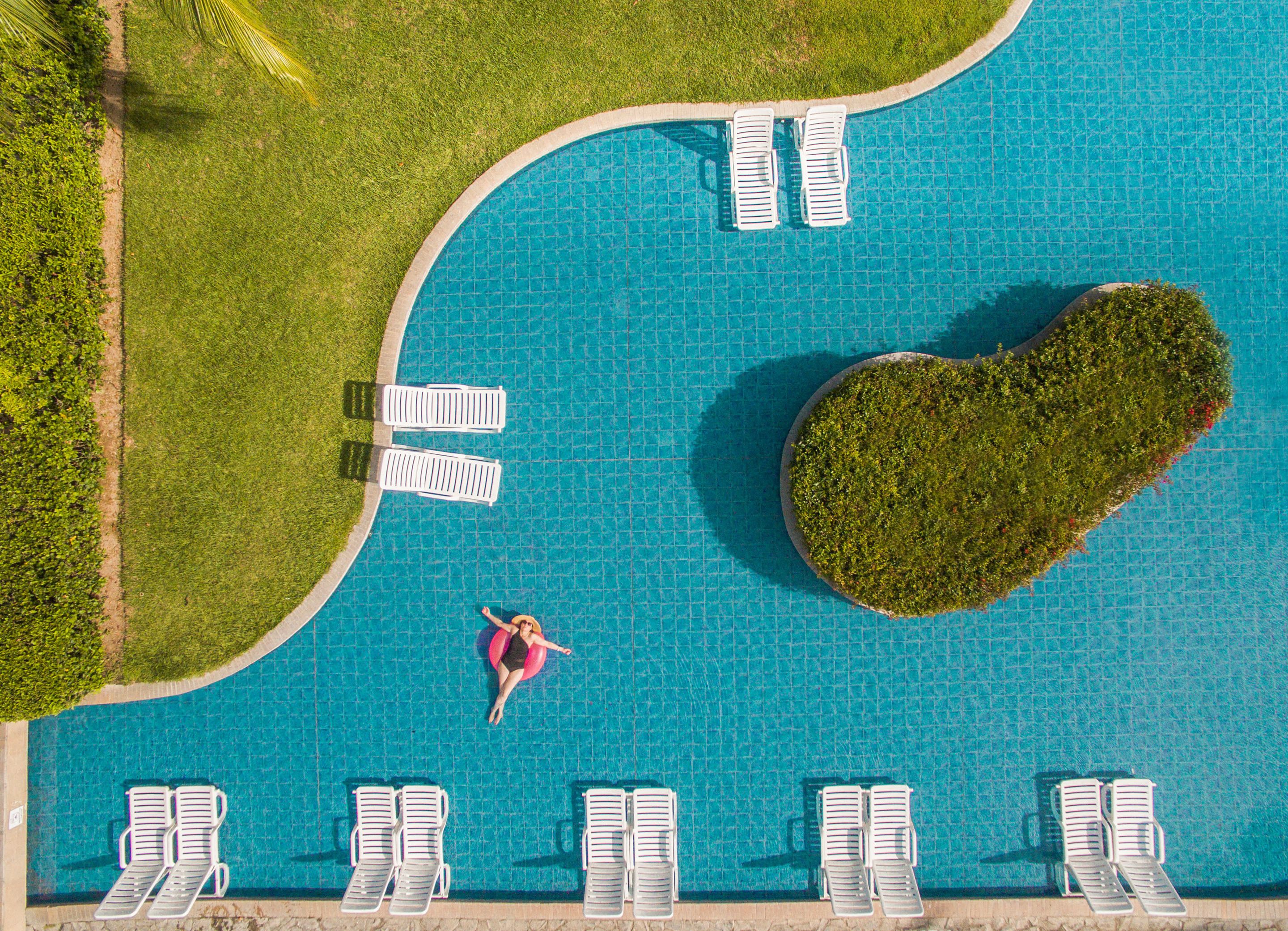 Vista aérea de una piscina con múltiples sillas de descanso y una isla con forma de corazón.