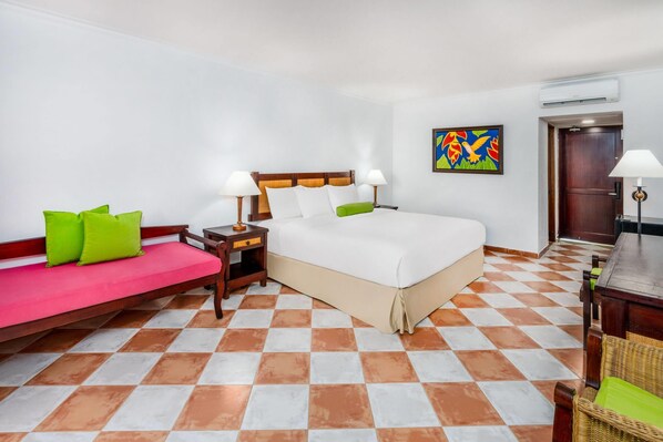 Une chambre d’hôtel avec un lit, un canapé, une table de chevet, une lampe et un tableau au mur.