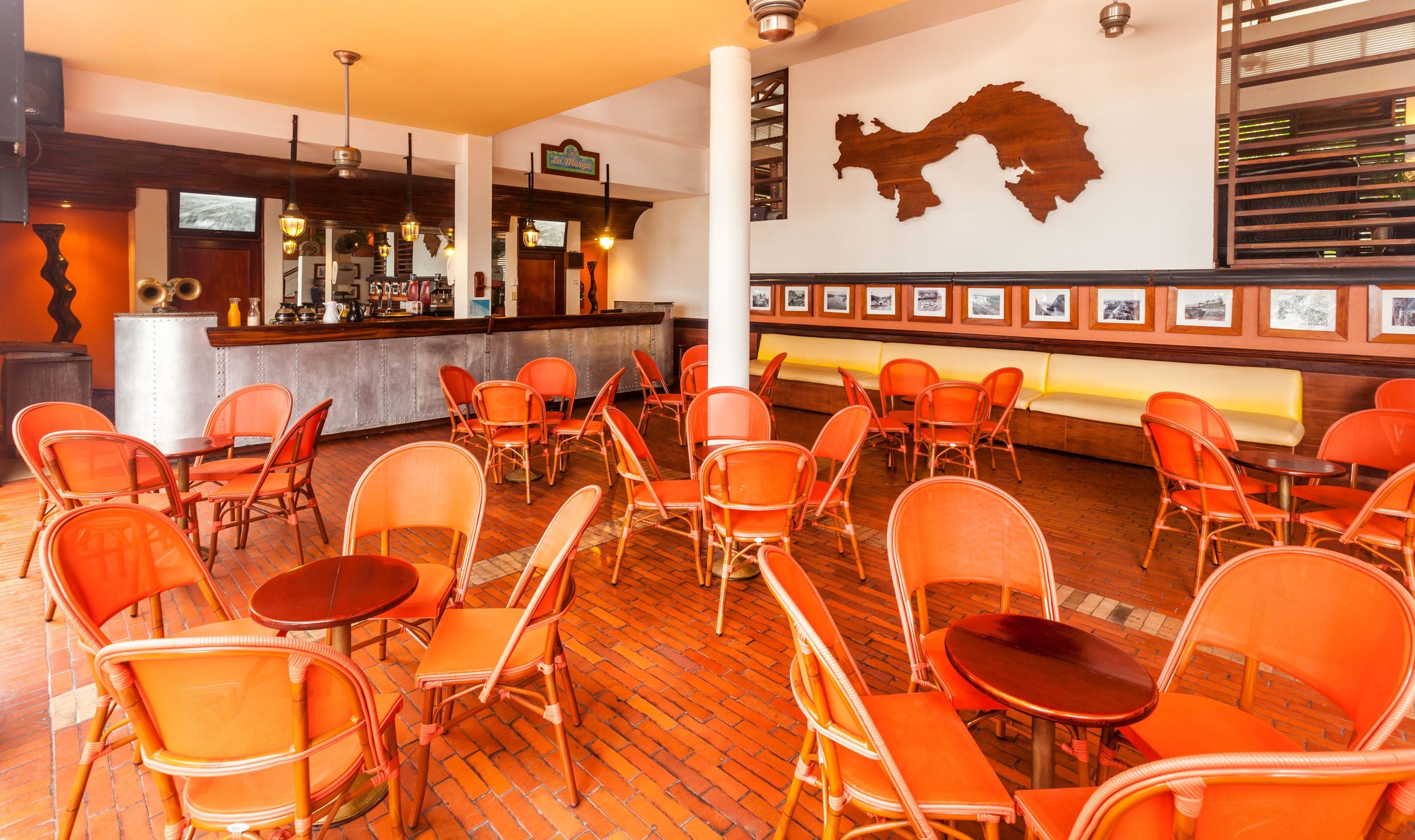A restaurant with wicker chairs and tables, a bar area, and a wall with framed pictures.