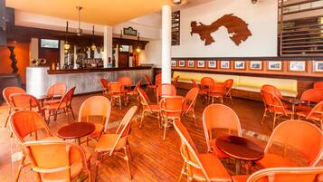 A restaurant with wicker chairs and tables, a bar area, and a wall with framed pictures.