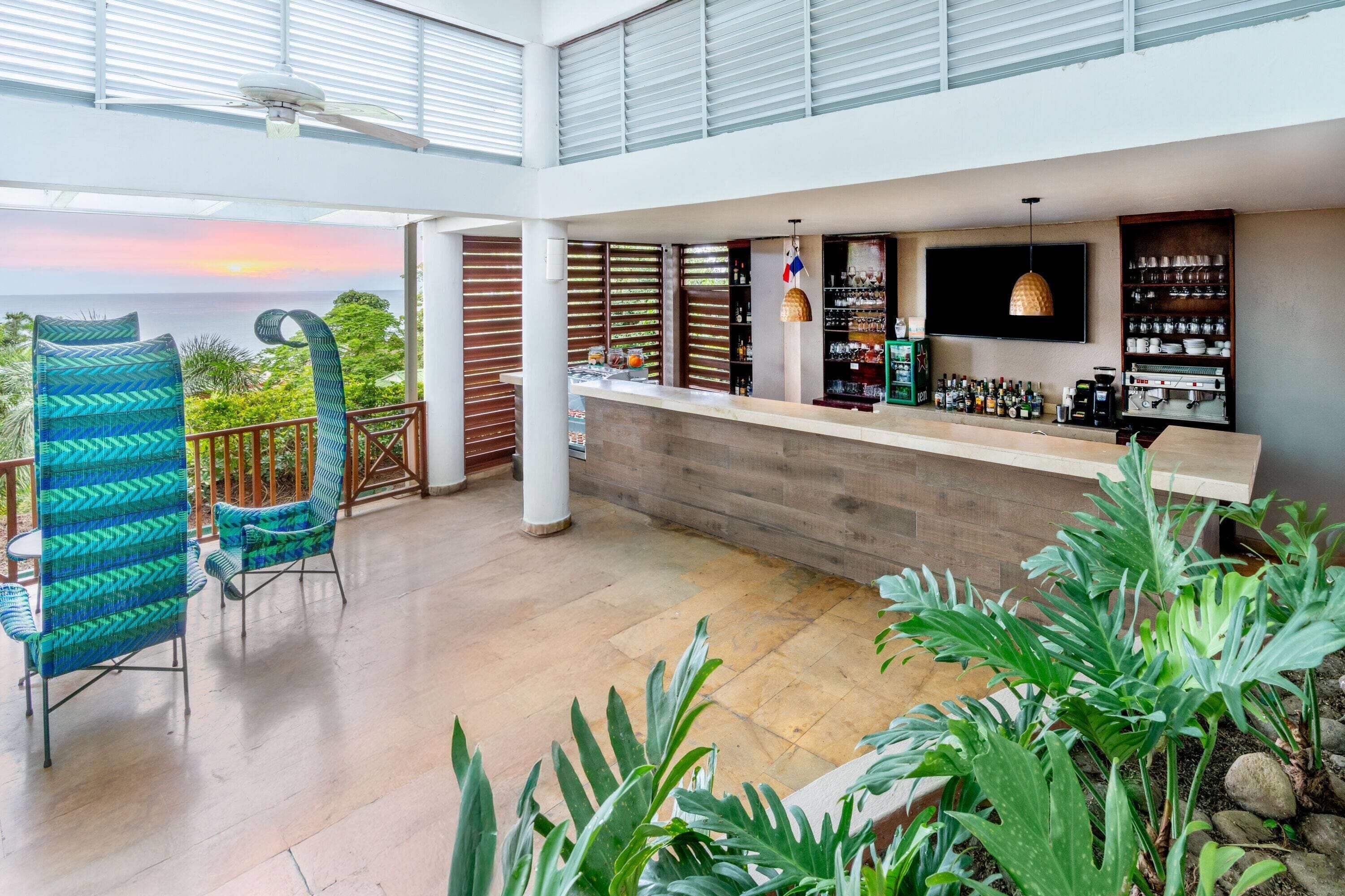 A modern bar area with a view of the ocean, featuring a counter, seating, and a variety of bottles and glasses.
