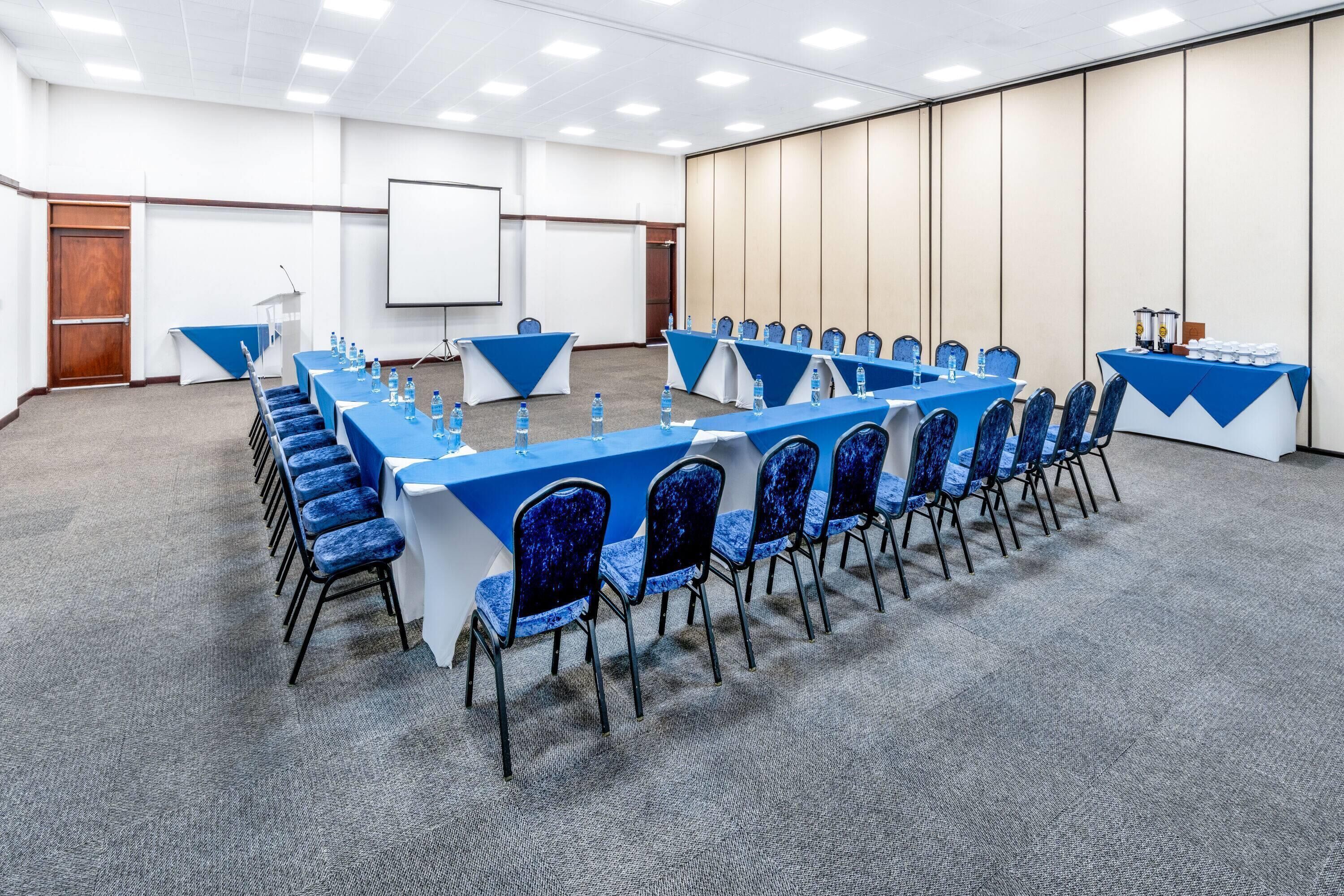 Ein Konferenzraum mit langem Tisch, blauen Stühlen und Wasserflaschen.