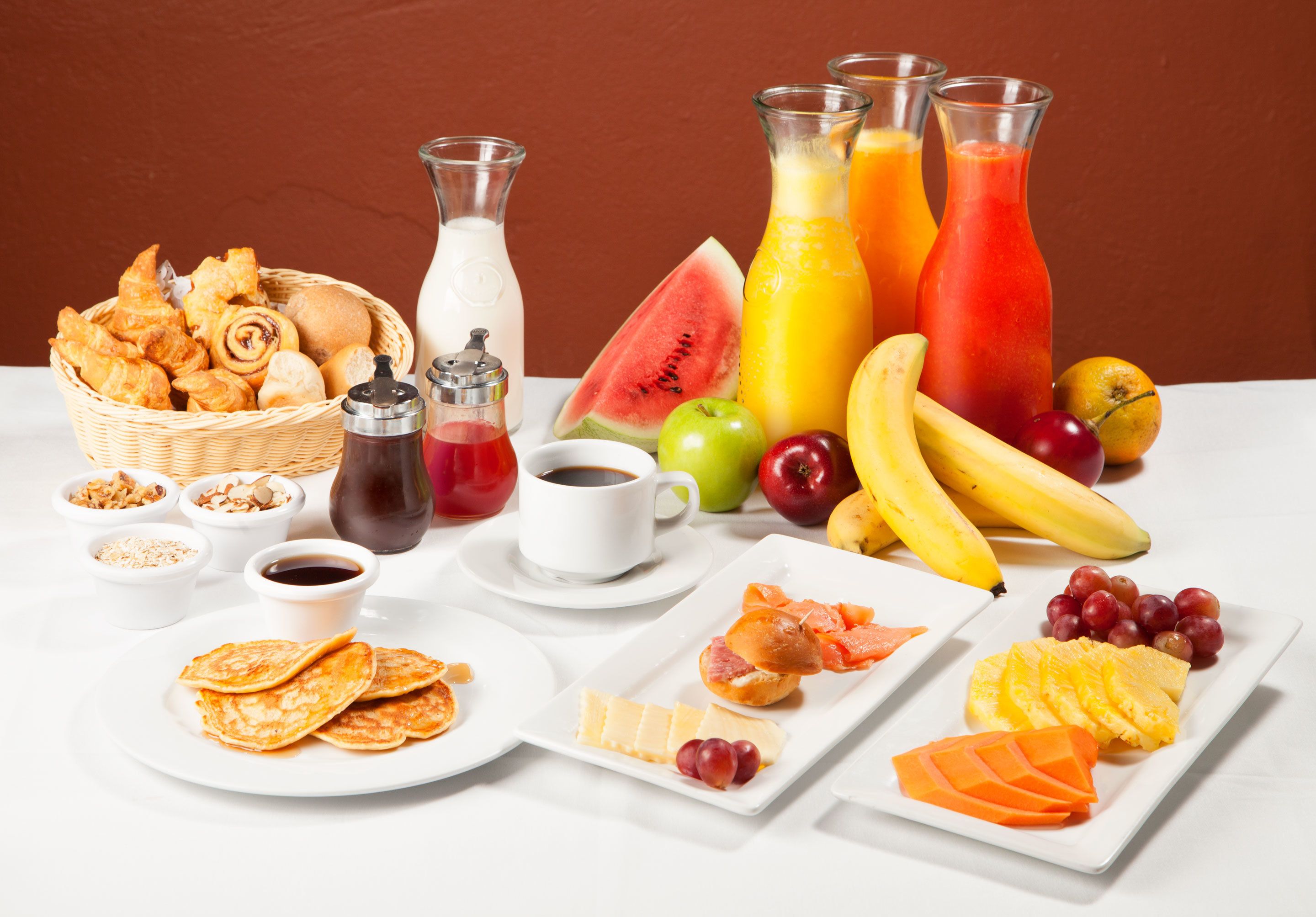 A breakfast spread with pastries, fruits, and beverages on a white table.
