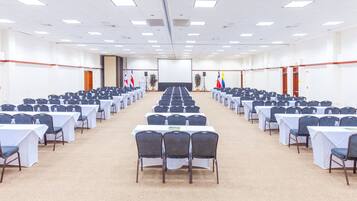 Uma sala de conferências com mesas e cadeiras dispostas em fileiras, uma tela de projetor e bandeiras.
