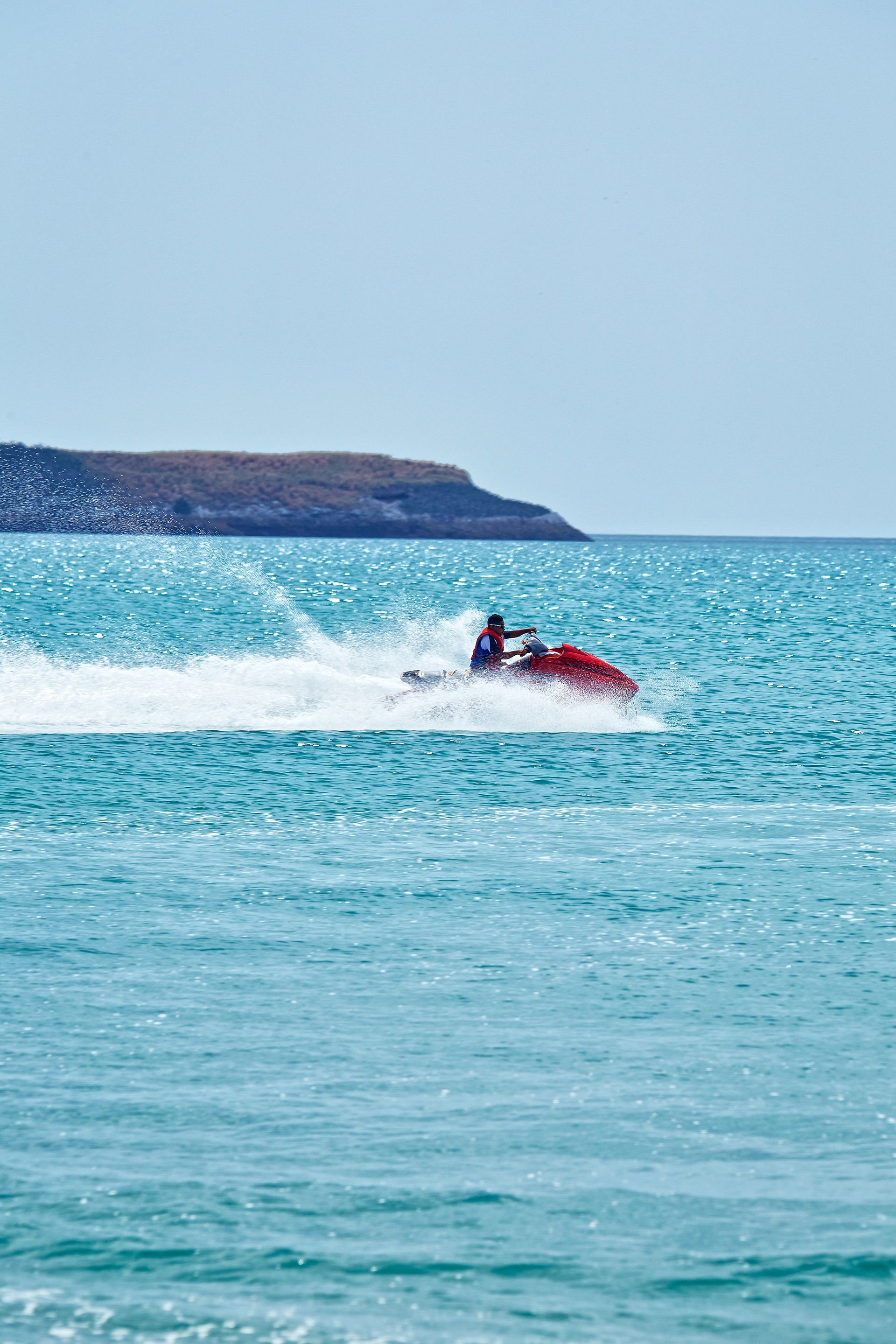A person jet-skiing on a clear blue sea with a distant landmass.