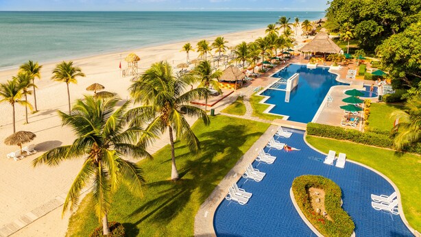 Un resort con piscina, playa y palmeras.
