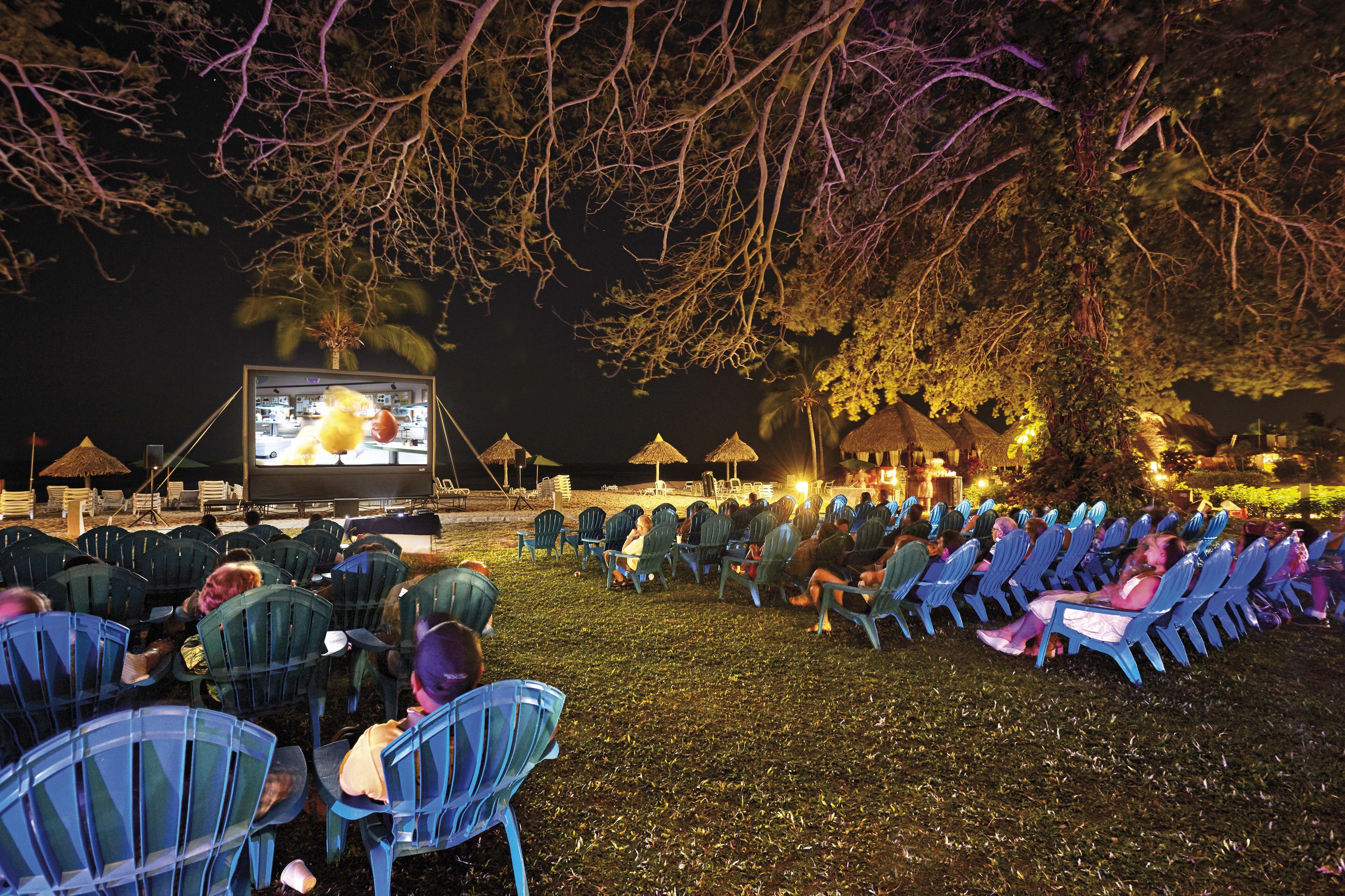 Un espace en plein air aménagé pour la projection de films, avec des rangées de chaises disposées face à un grand écran.