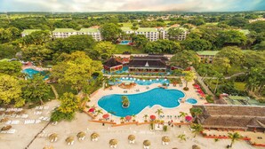 Vista aérea de un resort con varias piscinas, una zona de playa con tumbonas y abundante vegetación.