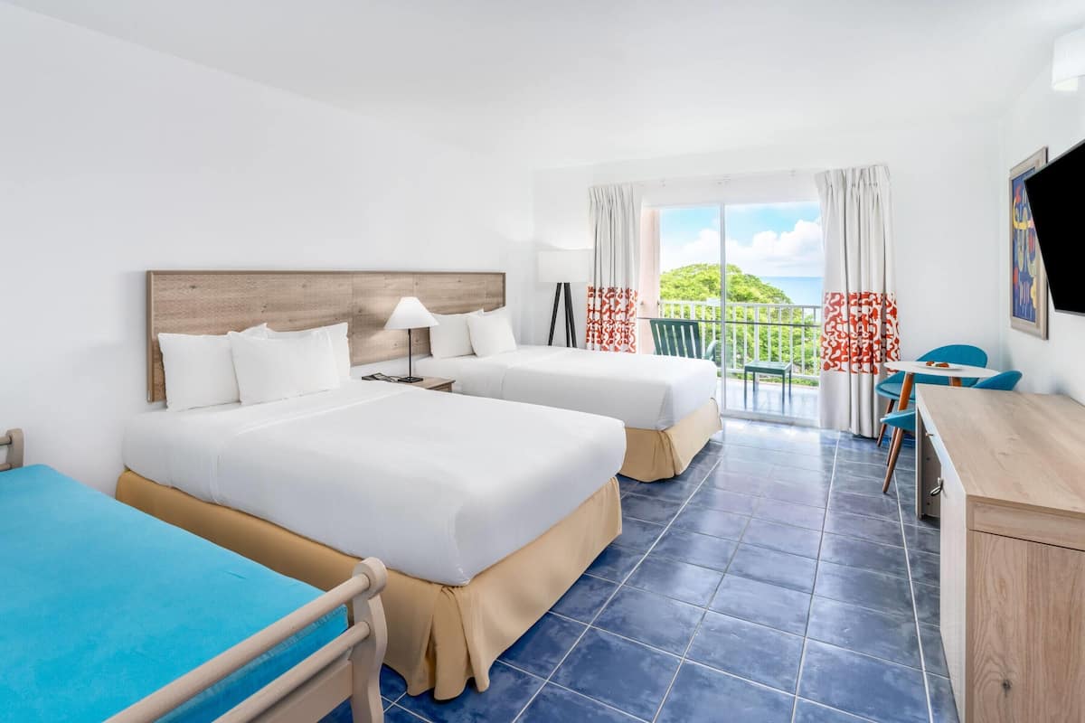 Een hotelkamer met twee bedden, een bureau, een stoel en een balkon met uitzicht op zee.