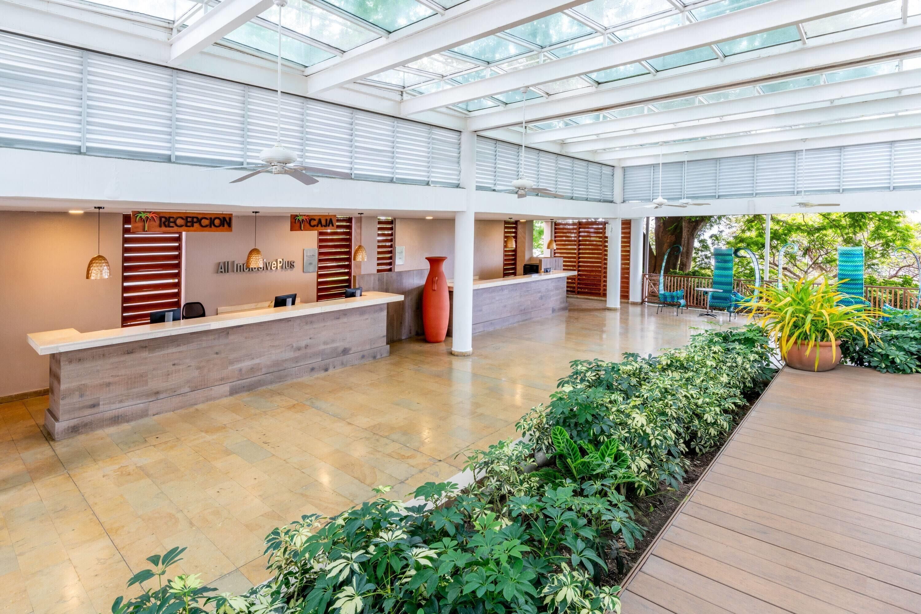 A spacious lobby with a reception desk, a ceiling fan, and a glass ceiling allowing natural light.