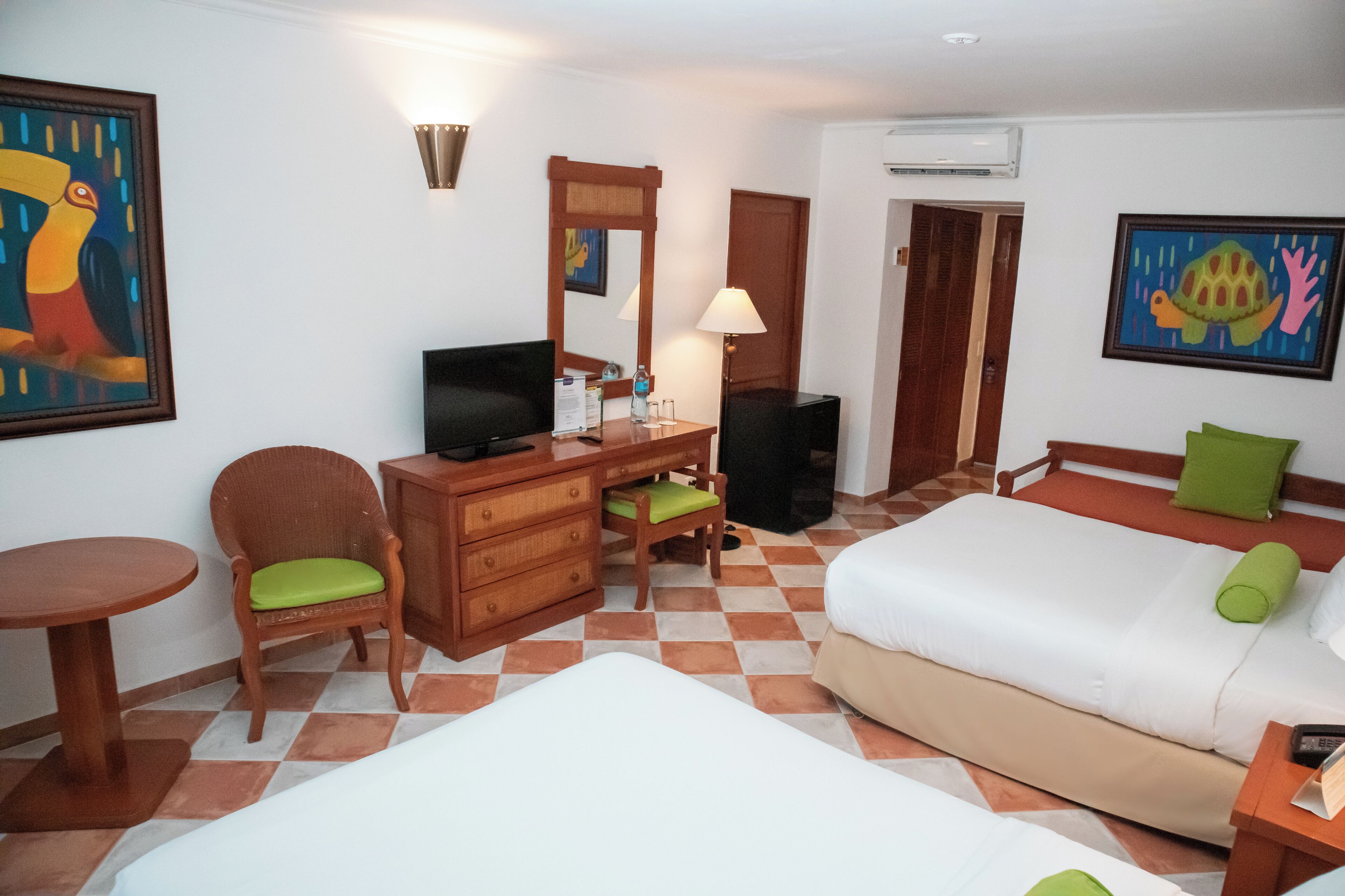 A hotel room with a bed, a desk with a chair, a television, a mirror, and a painting on the wall.