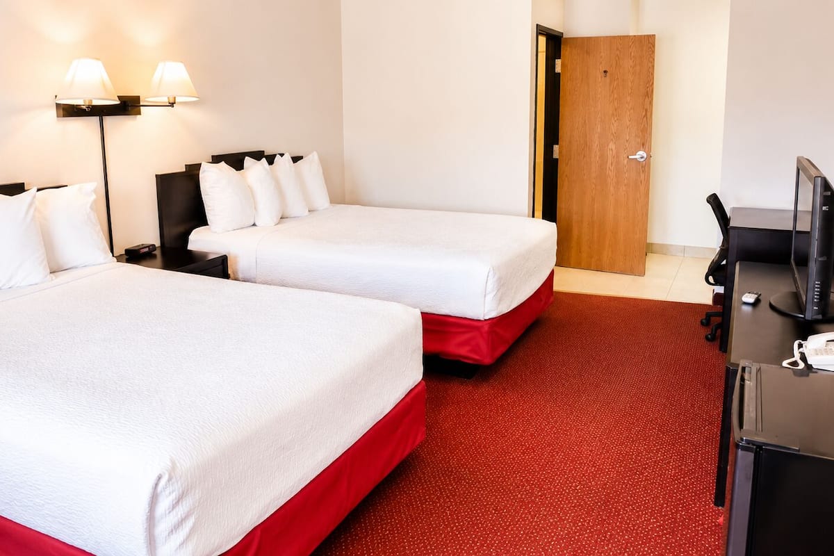 Habitació d'hotel amb dos llits, un escriptori amb un ordinador, un telèfon i una porta.