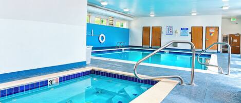 An indoor swimming pool with clear water, a lifeguard stand, and a blue tiled floor.