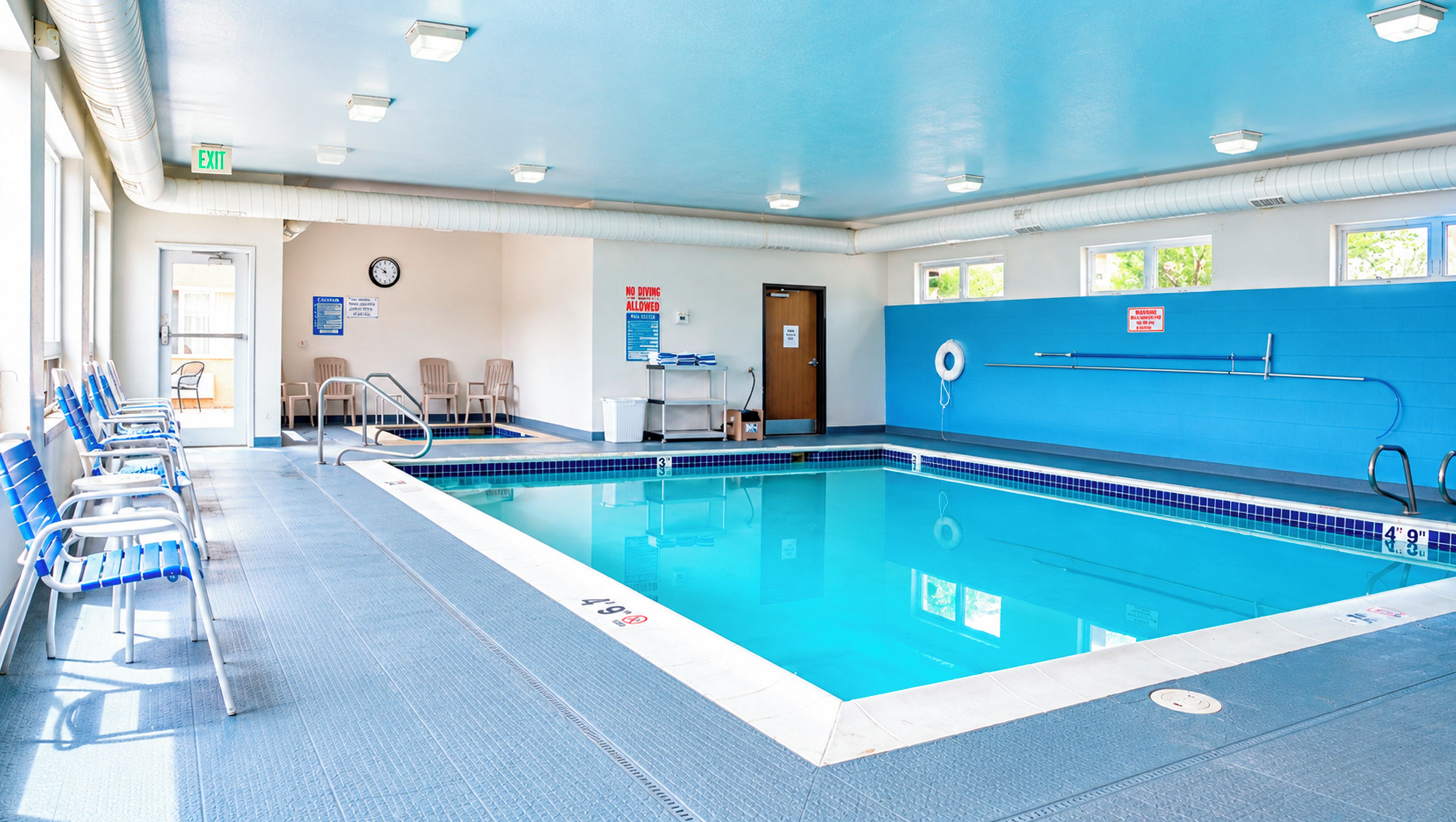 Una piscina interior con agua cristalina, borde de azulejos azules y una silla de salvavidas.