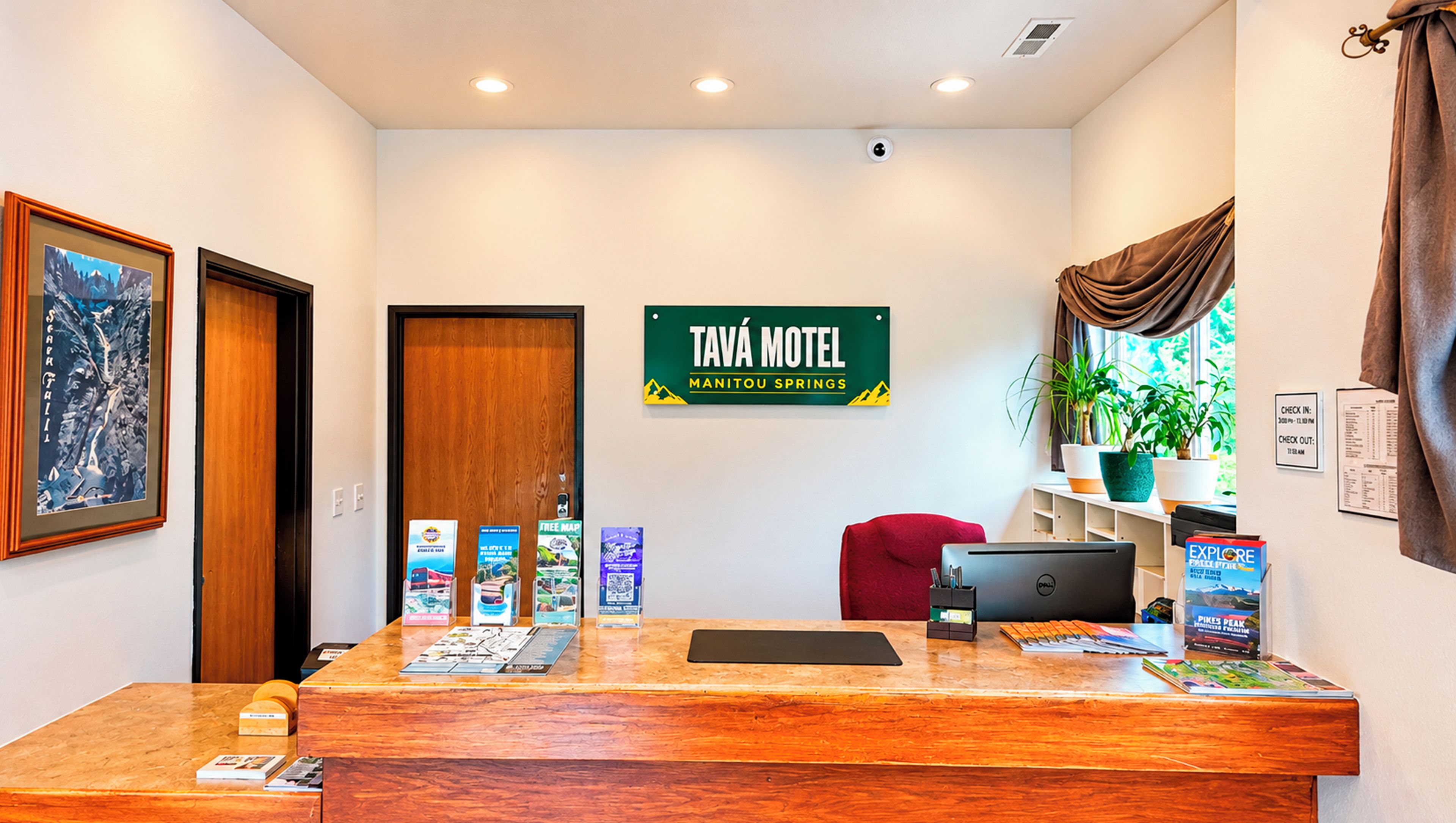 A reception desk with a sign for Tava Motel, a red chair, a laptop, and a plant.