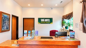 Un comptoir d’accueil avec une enseigne indiquant « Tava Motel », une chaise rouge, un ordinateur portable et une plante.