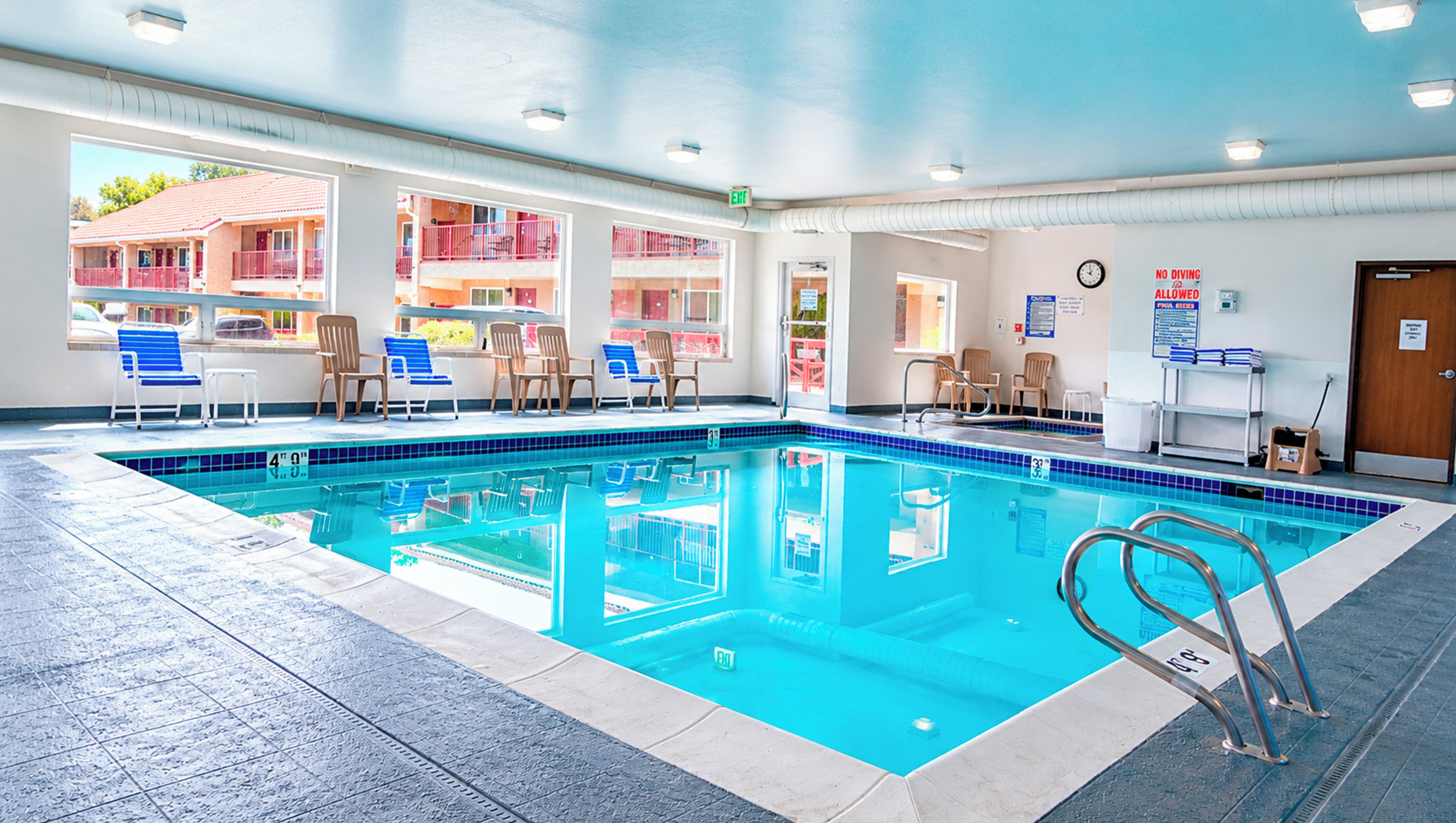 An indoor swimming pool with clear water, blue chairs, and a lifeguard chair.