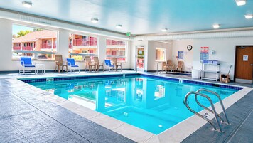Una piscina interior con agua cristalina, sillas azules y una silla para socorrista.