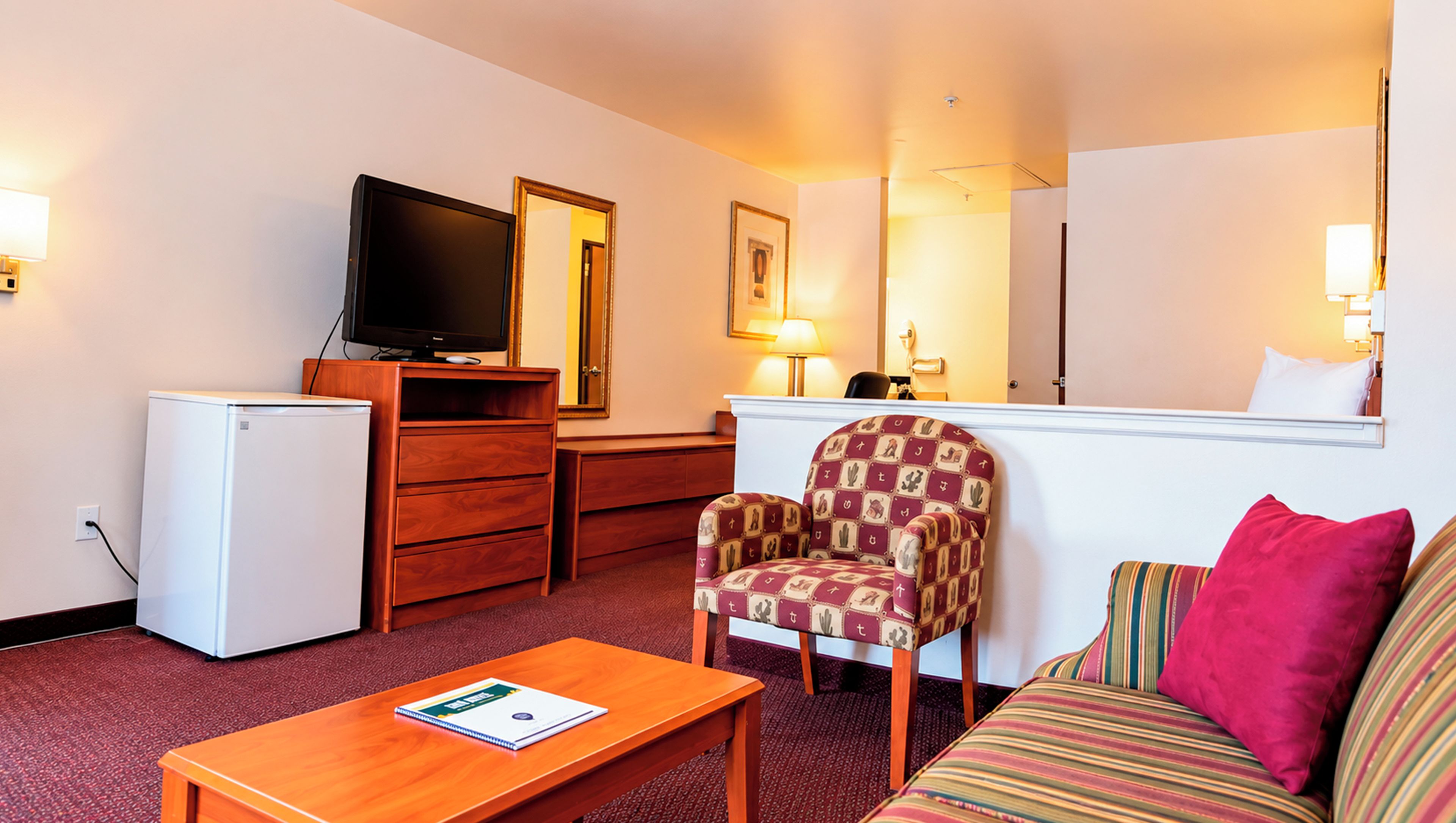 A hotel room with a television, a desk, a chair, a sofa, and a small table.