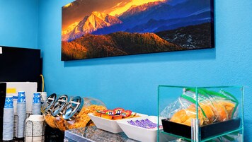 Habitación con un cuadro de paisaje de montaña, un mostrador de aperitivos con diferentes productos alimenticios y una vitrina de vidrio con pan.