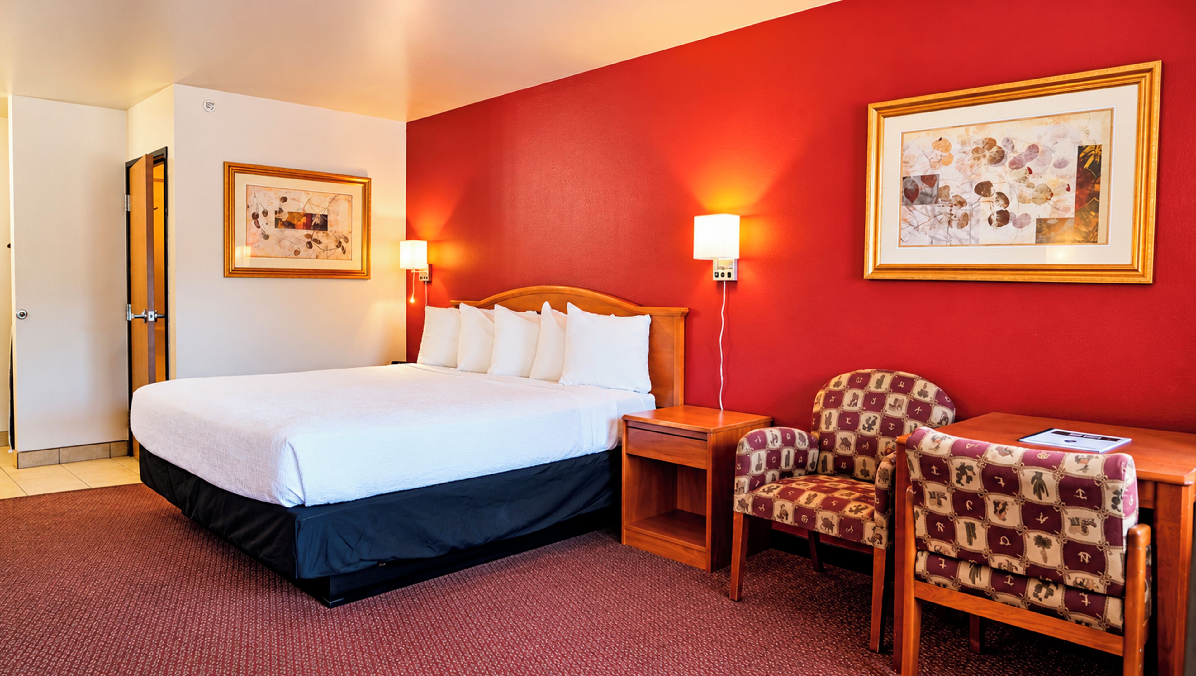 A hotel room with a large bed, two bedside tables, a chair, and two framed pictures on the walls.