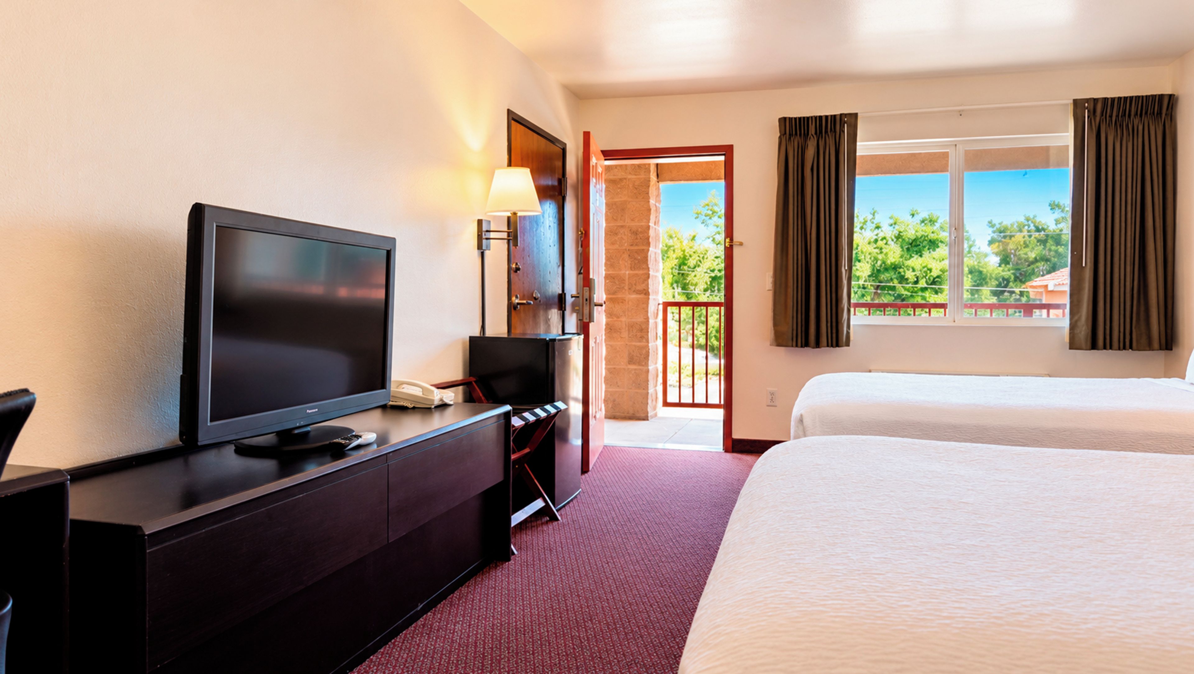 Ein Hotelzimmer mit Bett, Fernseher, Schreibtisch mit Telefon und einer Tür zu einem Balkon.