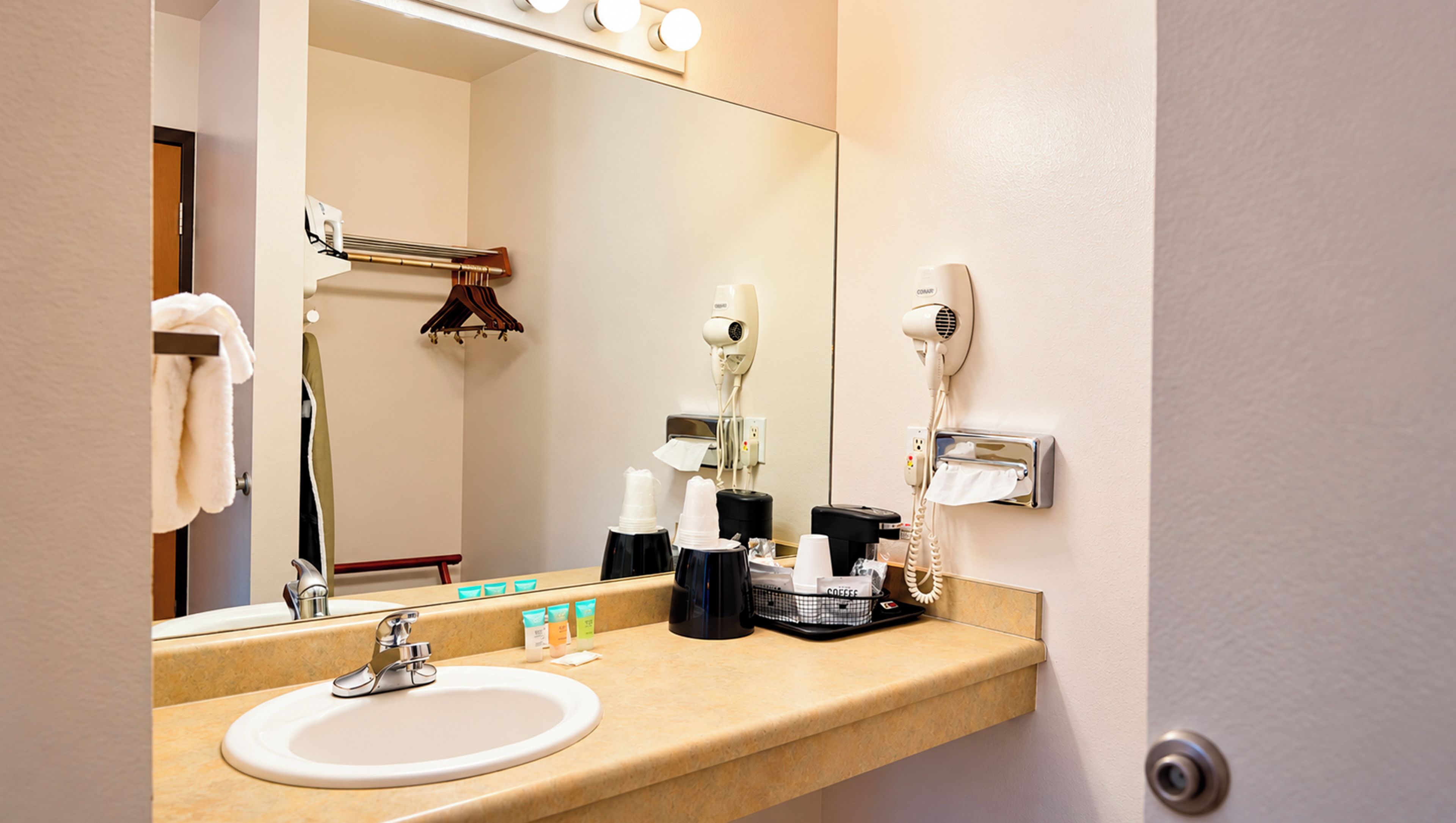 Une salle de bain d’hôtel équipée d’un lavabo, d’un miroir, d’un sèche-cheveux et d’un porte-serviettes.